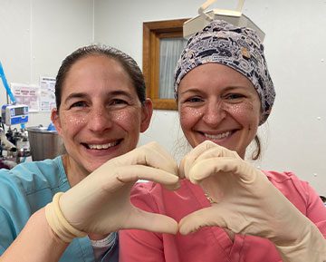 two female veterinarians wearing scrubs smiling and making a heart shape with hands